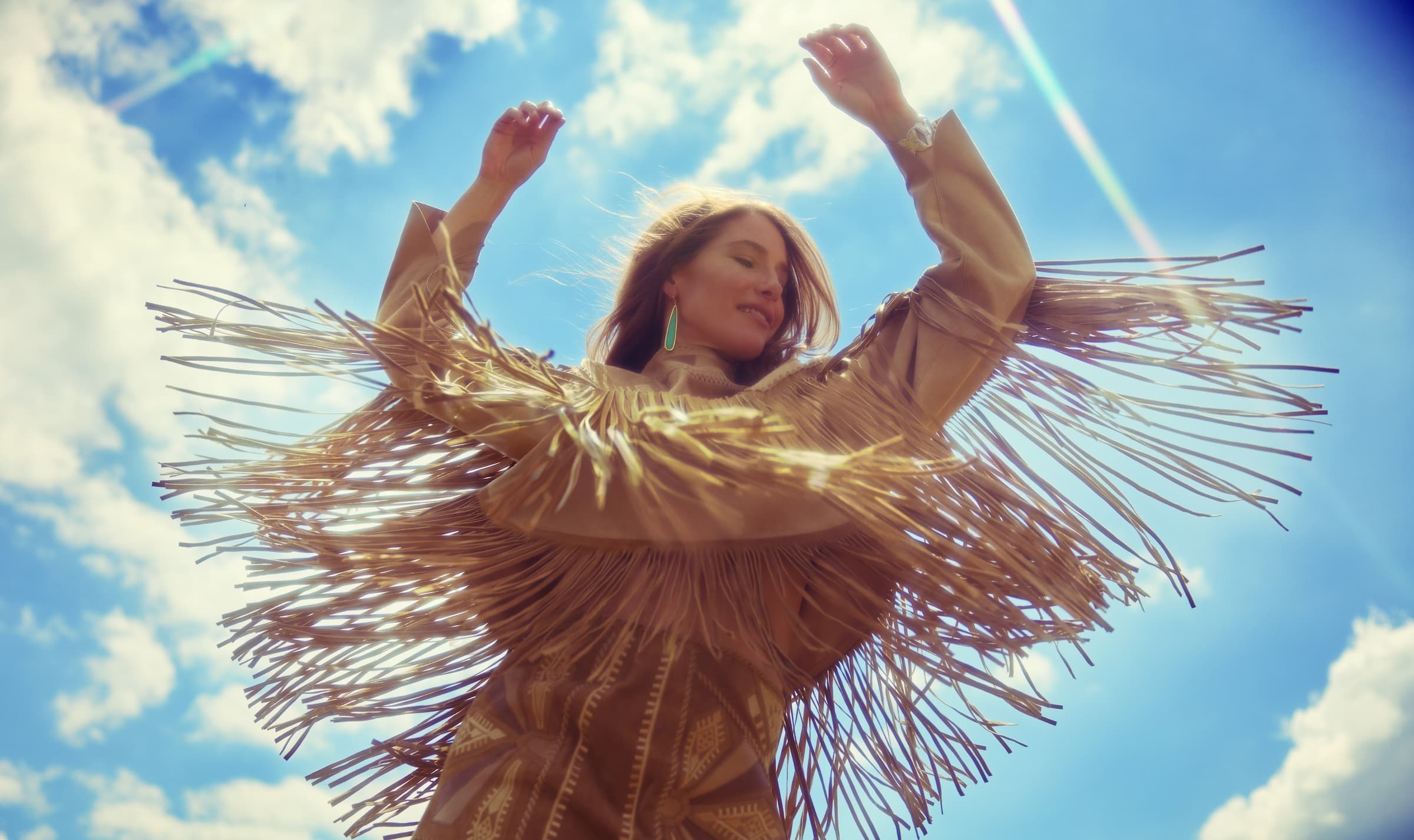 Caroline Jones in fringe jacket against a sun-drenched sky